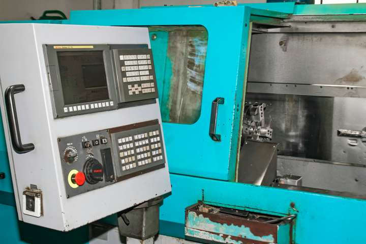 A CNC lathe with its door open and control panel lit, no operator at it