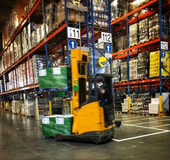 A forklift driving through a warehouse full of pallets