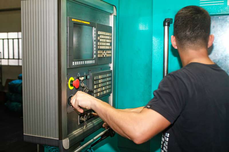 An operator, seen from behind, working the control panel of a CNC machine