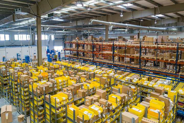 Order-picking zone in a logistics centre with rows of yellow totes and cartons by the racks