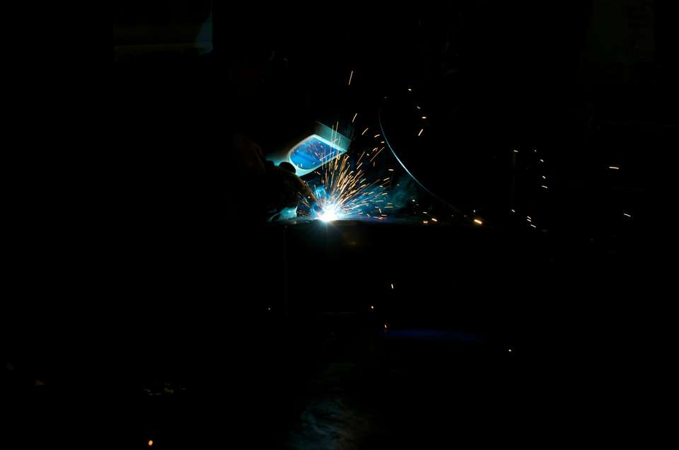 Welder at work, sparks flying in a dark workshop